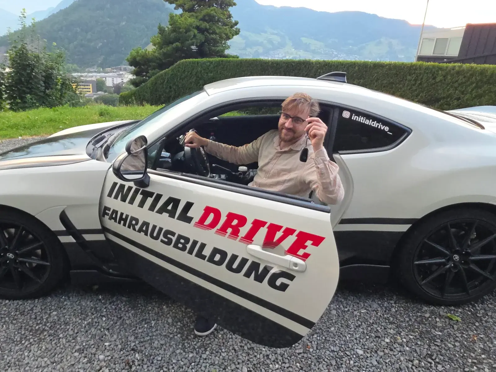Fahrlehrer Patrik Stadelmann sitzt im Toyota GR86 von Initial Drive und hält lächelnd den Autoschlüssel hoch