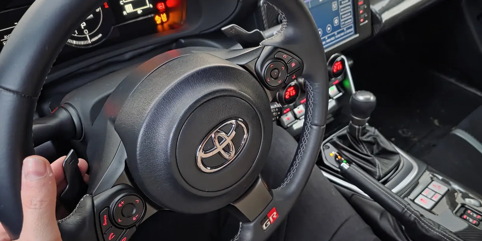 Hand am Lenkrad des Toyota GR86 der Fahrschule Initial Drive, rechts der Wählhebel des Automaten – Vorbereitung auf die Führerprüfung