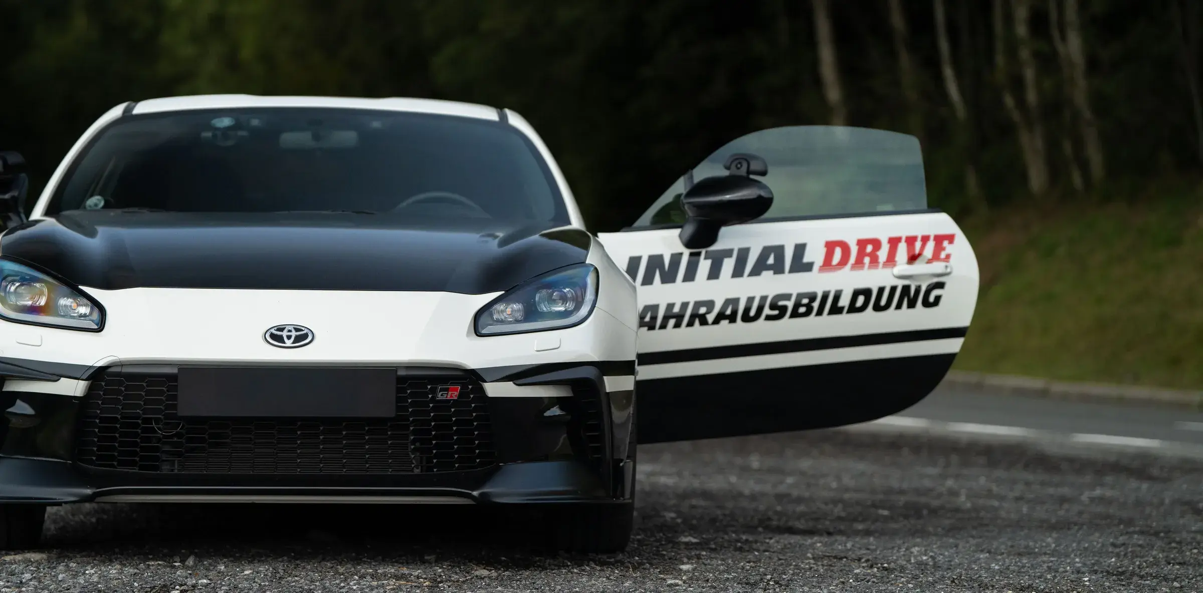 The Initial Drive Toyota GR86 from the front with its door open, “Initial Drive Fahrausbildung” on the door