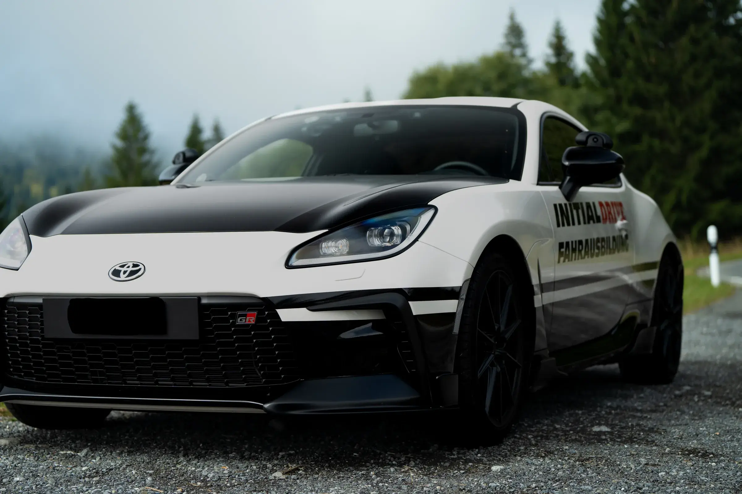 Toyota GR86 von Initial Drive von vorne, tief aufgenommen vor einem Waldrand