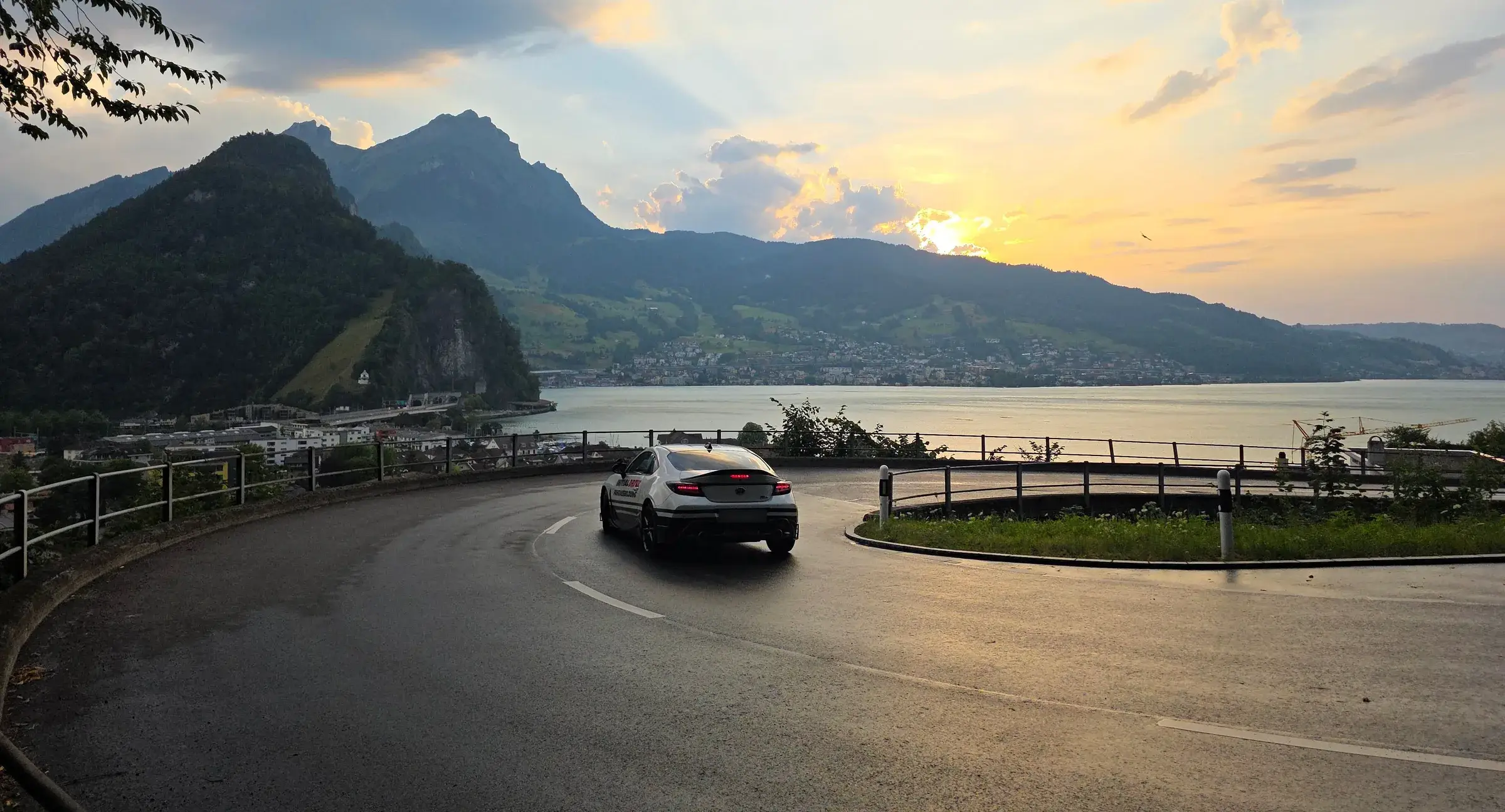 The Initial Drive Toyota GR86 turning into a hairpin bend above the lake in the evening light