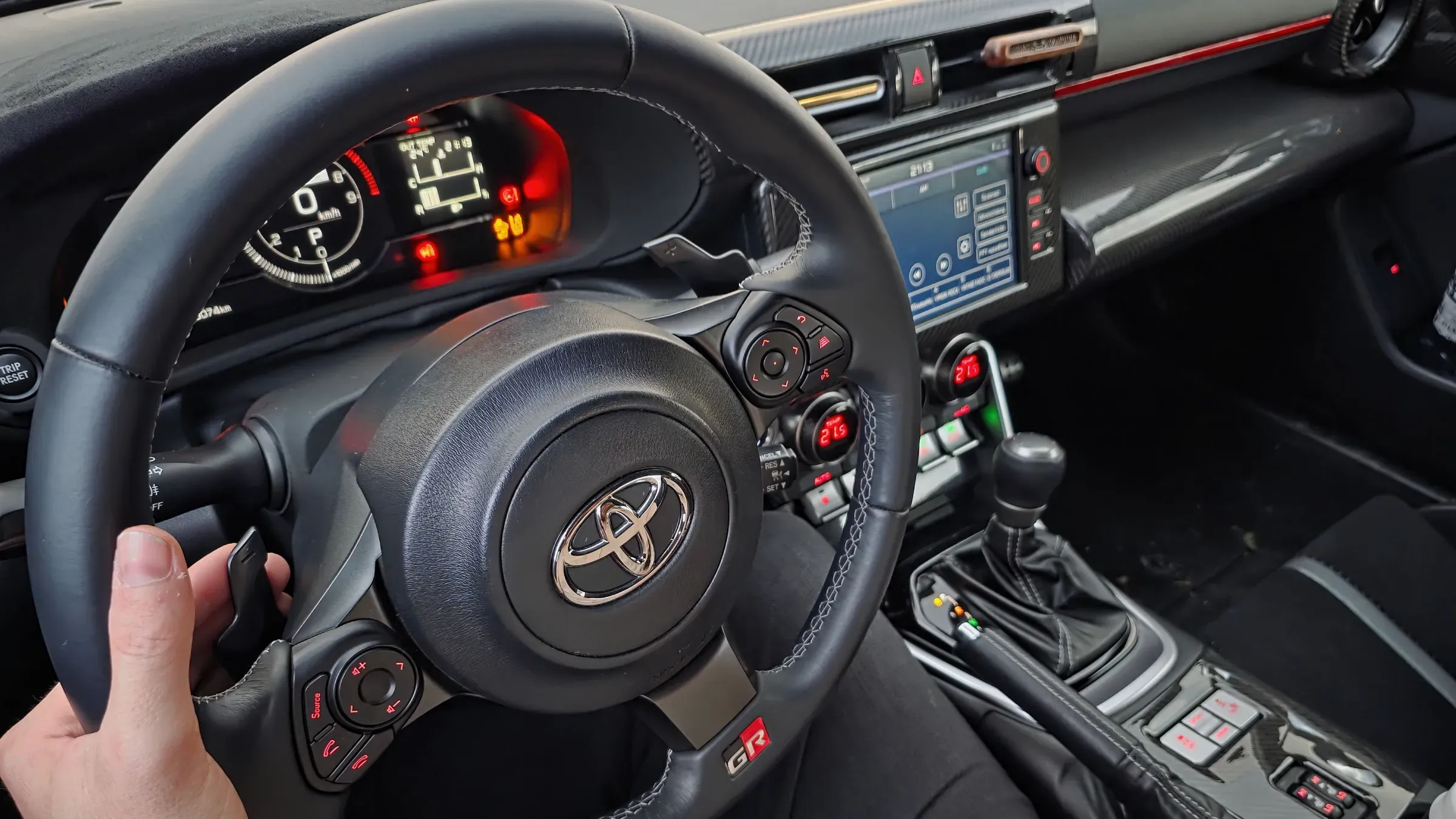Hand am Lenkrad des Toyota GR86 von Initial Drive, dahinter Instrumente und Wählhebel