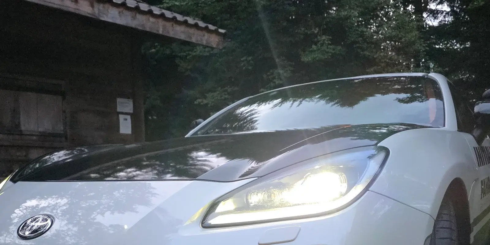 Toyota GR86 der Fahrschule Initial Drive mit eingeschalteten Scheinwerfern in der Dämmerung – Vorbereitung auf die Taxiprüfung BPT 121