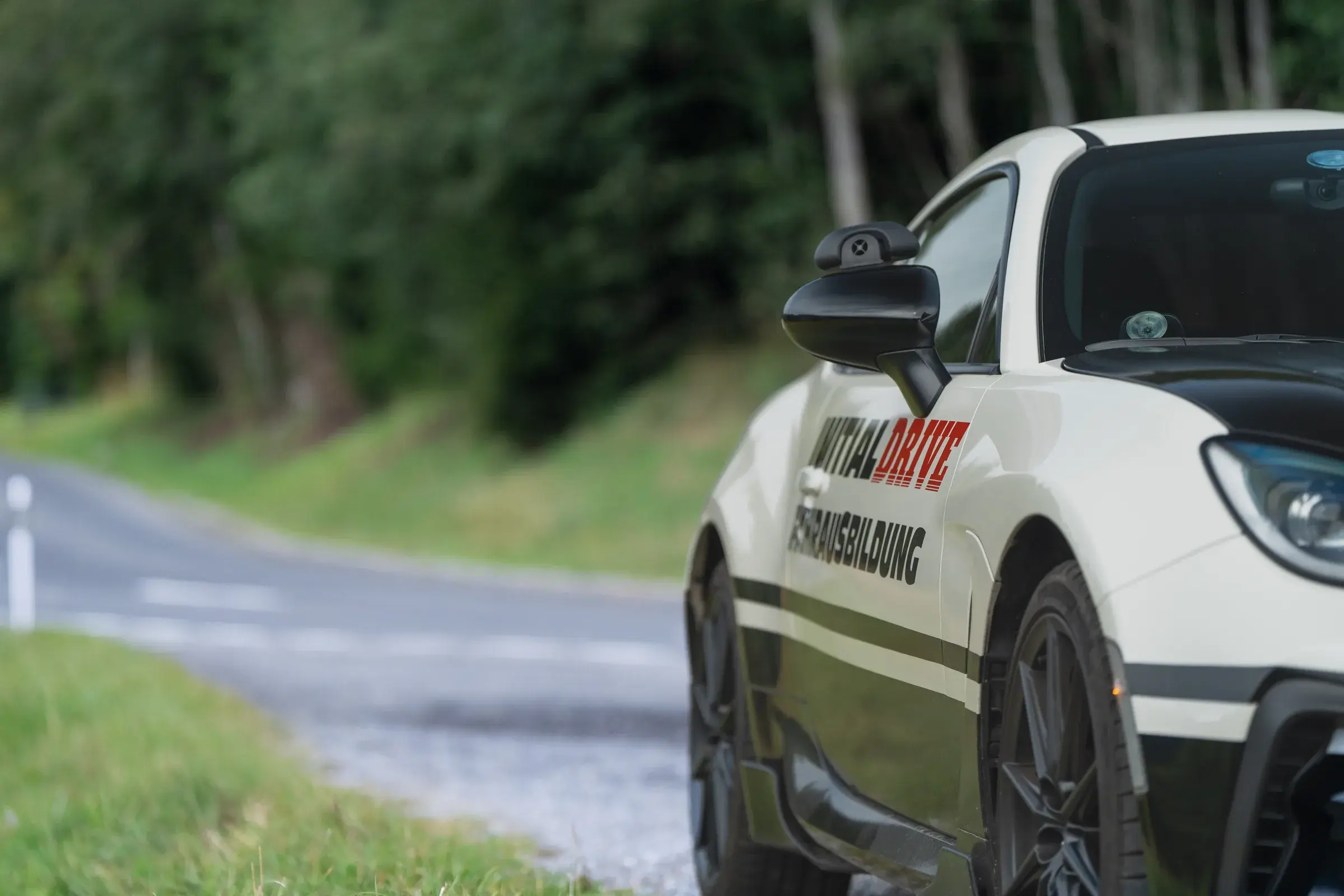 Toyota GR86 von Initial Drive mit Schriftzug an der Tür, dahinter eine Landstrasse am Waldrand
