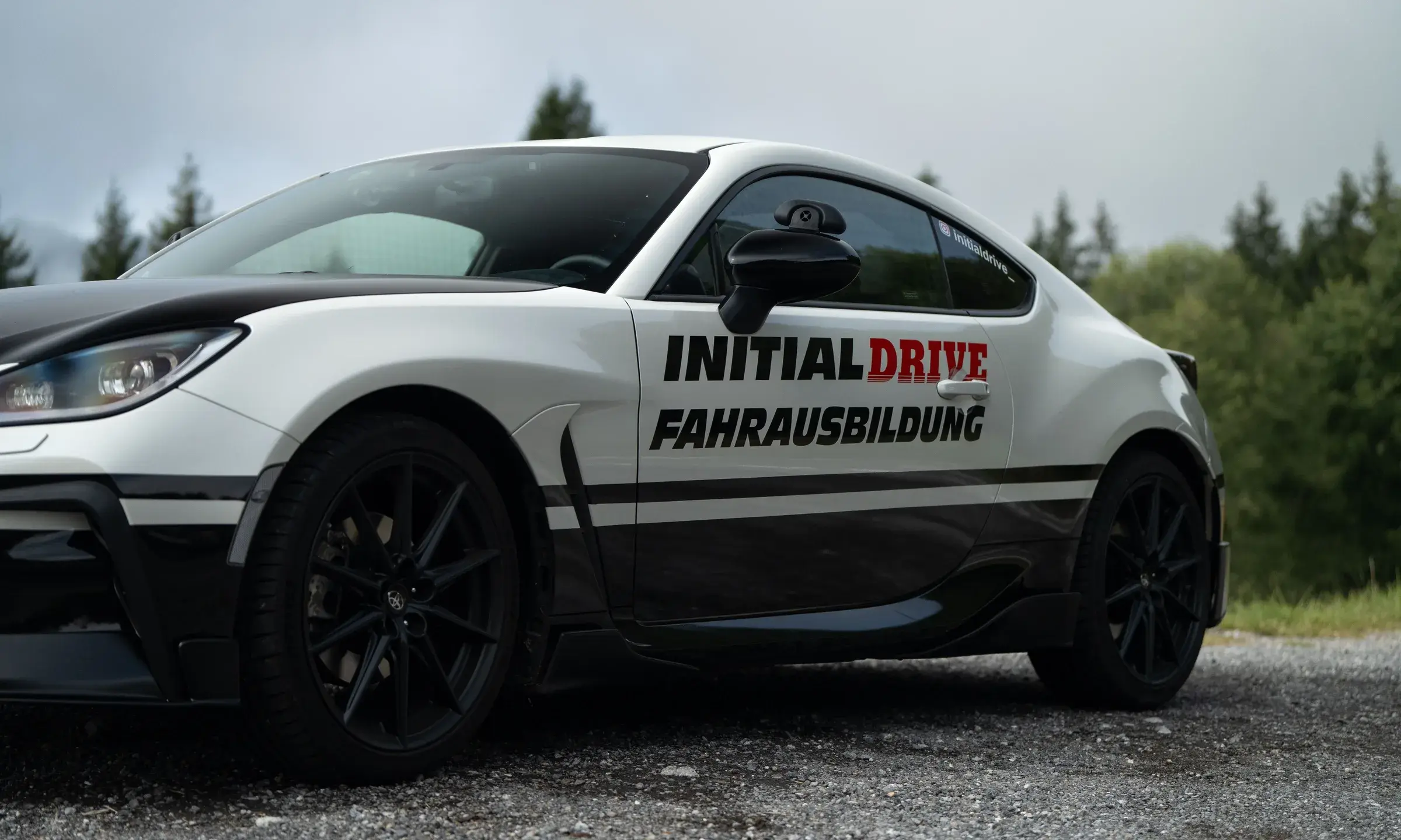 The Initial Drive Toyota GR86 from the front three-quarter view, with “Initial Drive Fahrausbildung” on the door